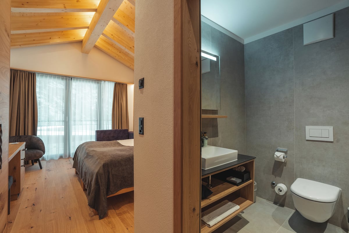A bedroom with a bed, a desk, and a chair. The room has wooden flooring and a sloped ceiling.