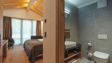 A bedroom with a bed, a desk, and a chair. The room has wooden flooring and a sloped ceiling.