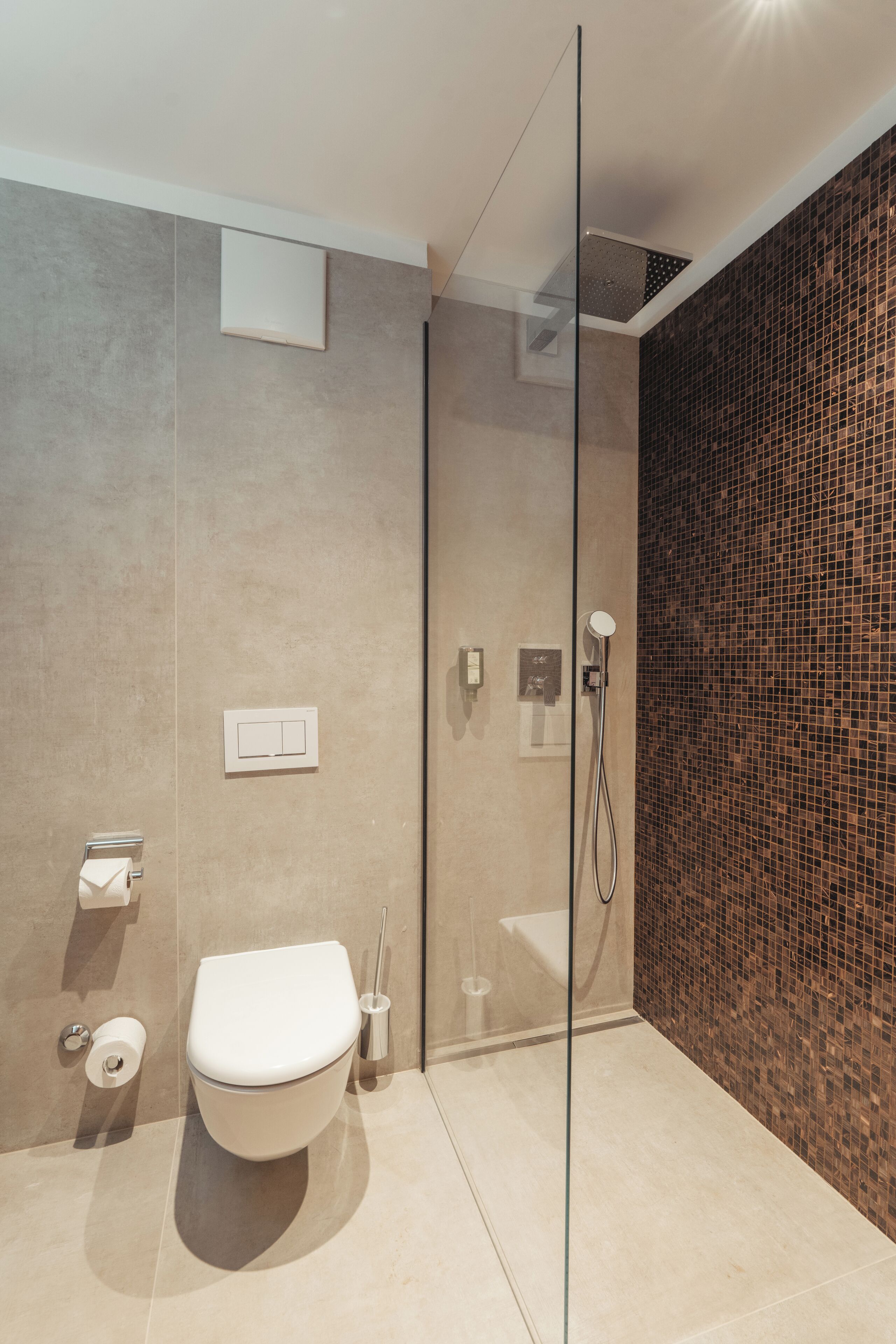 A modern bathroom with a glass shower enclosure, a toilet, and a tiled wall.