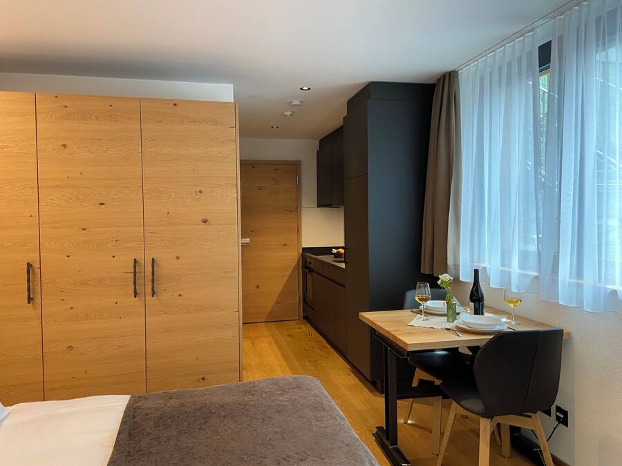 Une chambre moderne comprenant un lit, une table à manger avec des chaises, un coin cuisine et une grande armoire.