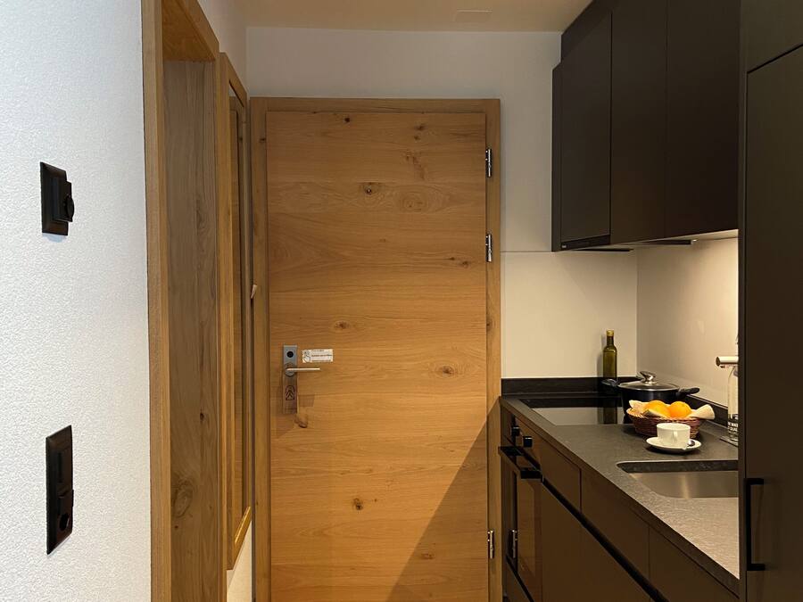 A modern kitchen with wooden flooring, a built-in oven, and dark cabinetry.