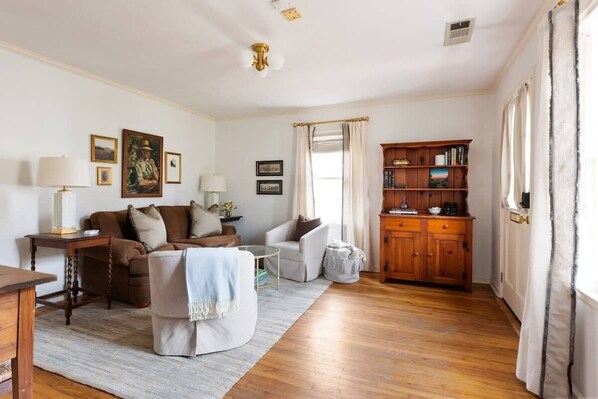 A living room with a sofa, armchairs, a wooden cabinet, and a dining table.