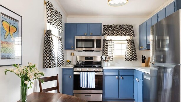 A kitchen with blue cabinets, a stainless steel refrigerator, a microwave, and a stove.