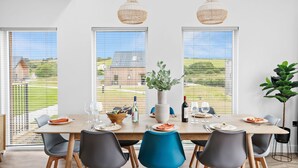 A dining area with a long table, chairs, and a potted plant. - 5 The Vista, Willingcott Nr Woolacombe - Hot tub/ Pet friendly/ On-site pool / Ecohome (Woolacombe)