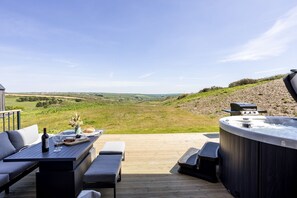 Eine Außenpatio mit Whirlpool, Sitzgelegenheiten und einem herrlichen Ausblick auf sanfte Hügel und Windkraftanlagen.