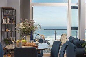 A dining area with a view of the ocean, a bookshelf, and a vase with flowers. - The Penthouse, Forty Eight Ocean 1 - spacious penthouse with balcony and sea views (Newquay)