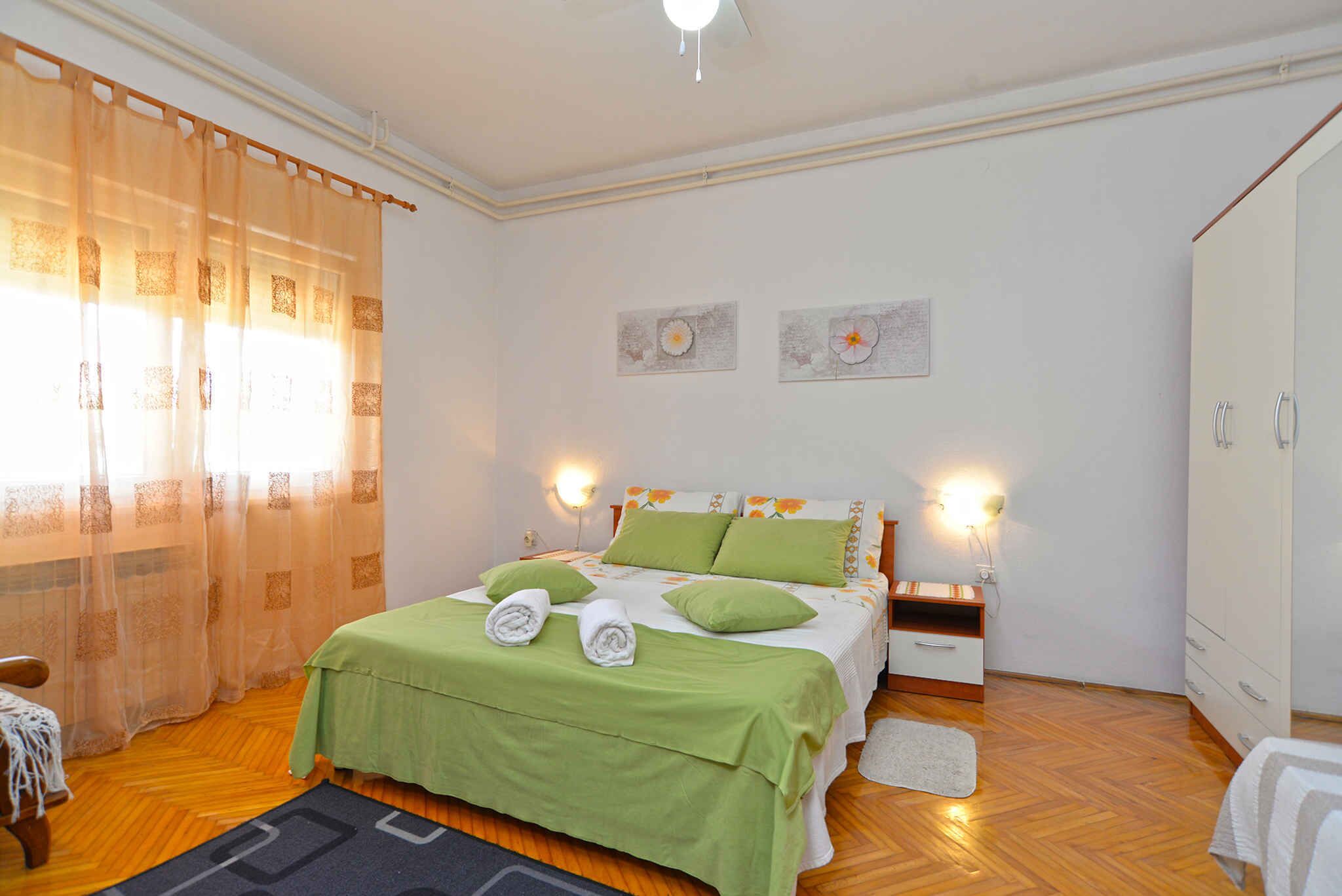 A bedroom with a bed, green bedding, two wall-mounted lamps, and a wooden floor.