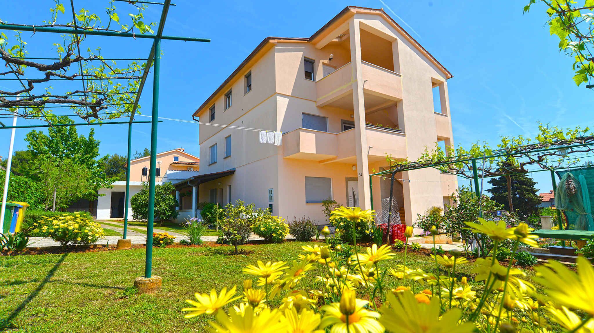 Un edificio residencial de varios pisos con balcones, rodeado de un jardín bien cuidado con flores amarillas.