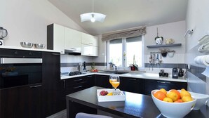 A modern kitchen with dark cabinetry, a built-in oven, a large island with a glass of orange juice, and a bowl of oranges. - Holiday apartment with sea view and air conditioning (Banjole)