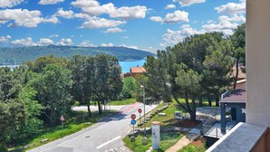 A road with a stop sign, a blue directional sign, and a view of a body of water and hills in the distance. - Holiday apartment with sea view and air conditioning (Banjole)