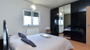 A bedroom with a bed, a window, a radiator, a chair, and a wardrobe. - Holiday apartment with sea view and air conditioning (Banjole)