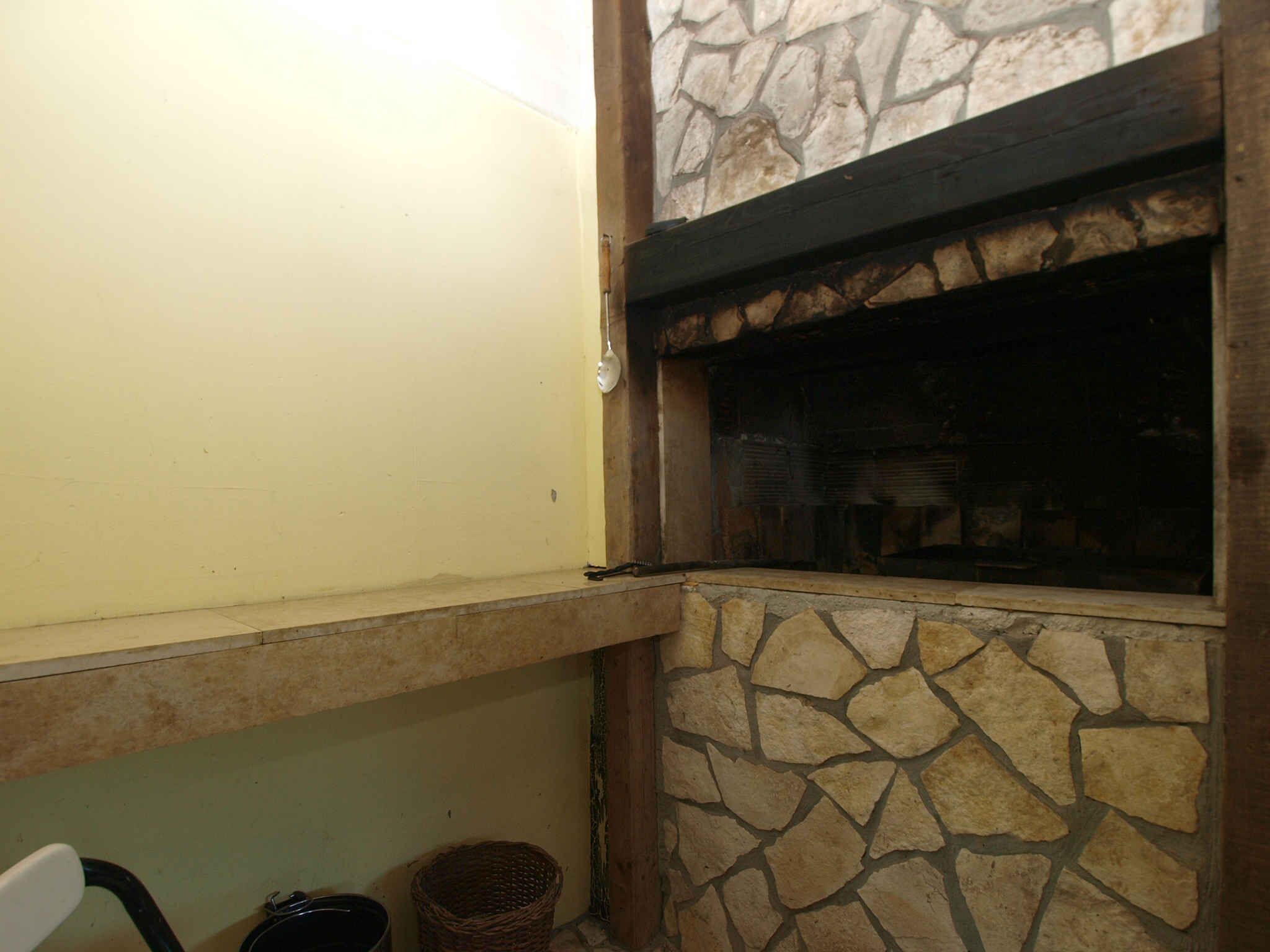 Une cheminée en pierre avec un manteau en bois, un mur jaune et une fenêtre.