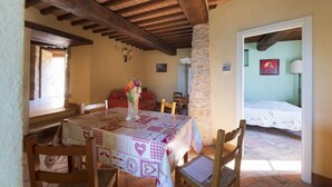 A dining area with a table set for two, a stone pillar, and a view into a bedroom with a bed and a nightstand. - Appartamento Ampio nel Borgo Medioevale (colle di val d'elsa)