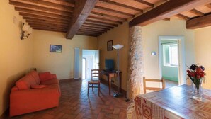 A cozy living room with a red sofa, a dining table with a vase of flowers, and a stone pillar. - Appartamento Ampio nel Borgo Medioevale (colle di val d'elsa)