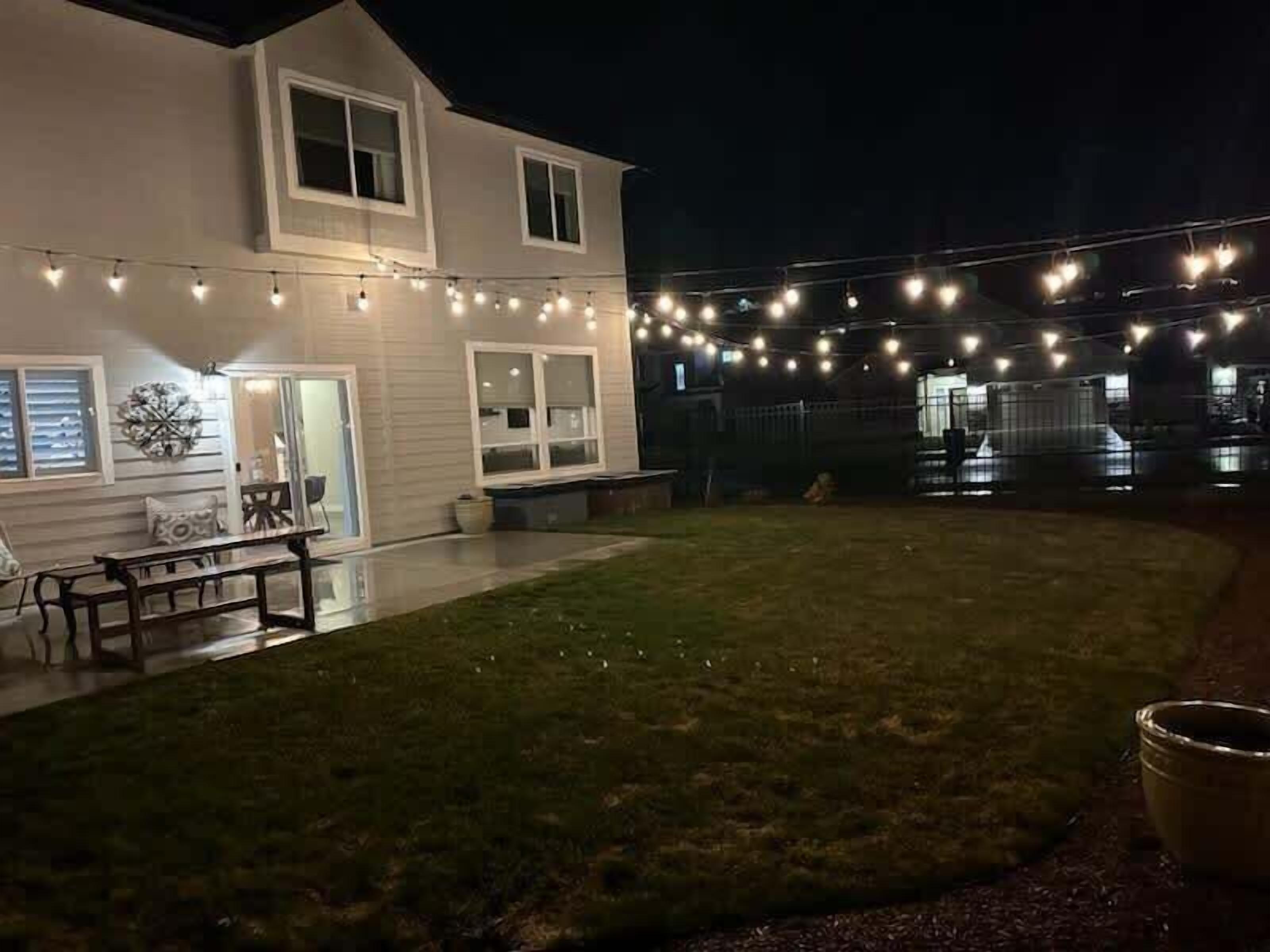 Une maison blanche avec une pelouse, des guirlandes lumineuses et un banc.
