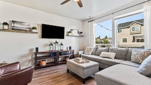 A modern living room with a flat-screen TV, wooden entertainment unit, grey sofa, and a ceiling fan.