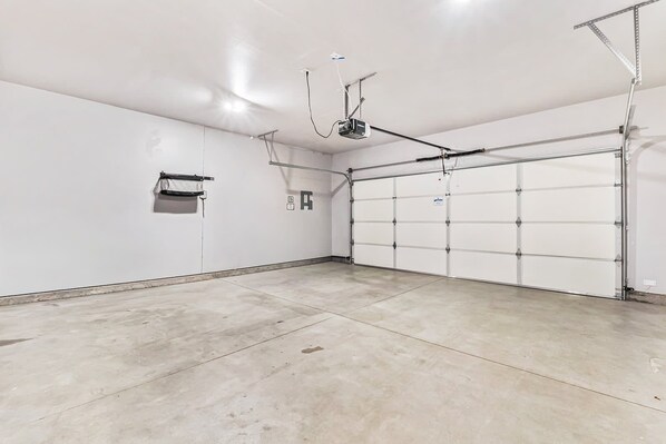 Un garage propre et vide, avec une porte blanche, un projecteur fixé au plafond et une boîte électrique fixée au mur.