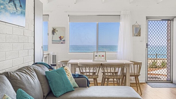 Ein gemütliches Wohnzimmer mit einer Couch, einem Esstisch und Stühlen. Ein großes Fenster bietet Blick auf das Meer.
