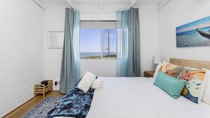 Ein Schlafzimmer mit einem großen Bett, Meerblick durch ein Fenster und einem Gemälde an der Wand.