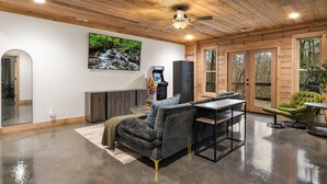 Una sala de estar moderna con un sofá gris, una mesita pequeña y un sillón verde. Hay un ventilador de techo, un ventanal grande y una puerta que da al exterior.