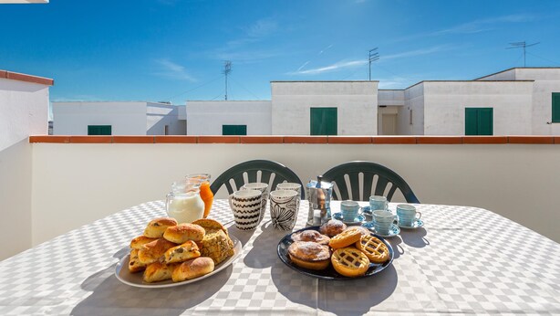 A table set with pastries and drinks on a balcony with a clear sky and buildings in the background. - 3712 Blusea Beach Apt - Primo Piano by Barbarhouse (Manduria)