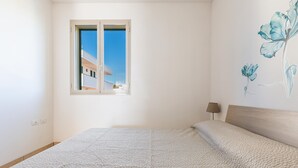 A bedroom with a large bed, a window with a view of a building, and a wall with a floral mural. - 3712 Blusea Beach Apt - Primo Piano by Barbarhouse (Manduria)