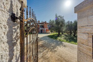 A gated entrance to a property with a stone wall, a metal gate, and a building in the background. - Holiday apartment with air conditioning (Rovinj)