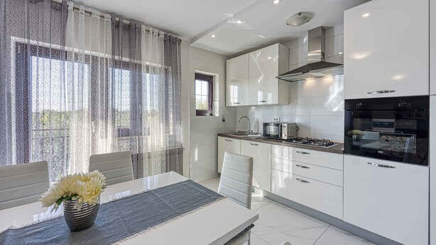 Une cuisine moderne avec des meubles blancs, une cuisinière à gaz et un four noir. On y trouve une table à manger avec des chaises et un vase rempli de fleurs.