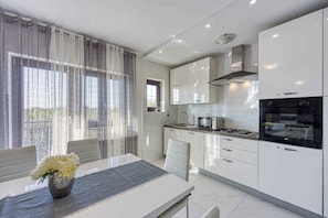 A modern kitchen with white cabinets, a gas stove, and a black oven. There is a dining table with chairs and a vase of flowers.