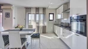 Une cuisine moderne équipée d’appareils électroménagers en acier inoxydable, un coin repas avec une table et des chaises, et une fenêtre avec des rideaux.