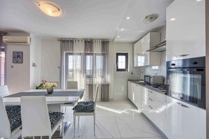 A modern kitchen with stainless steel appliances, a dining area with a table and chairs, and a window with curtains. - Holiday apartment with air conditioning (Rovinj)