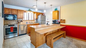 A kitchen with wooden cabinets, a stainless steel refrigerator, a built-in oven, and a wooden island with a bench.