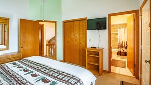 Un dormitorio con cama, armario de madera, televisión y baño visible a través de una puerta abierta.