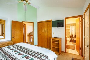 A bedroom with a bed, a wooden wardrobe, a television, and a bathroom visible through an open door.
