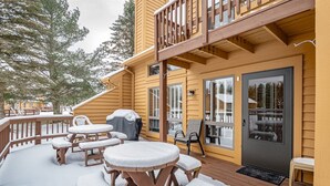 A wooden deck with outdoor seating and a covered grill area, surrounded by snow-covered trees.