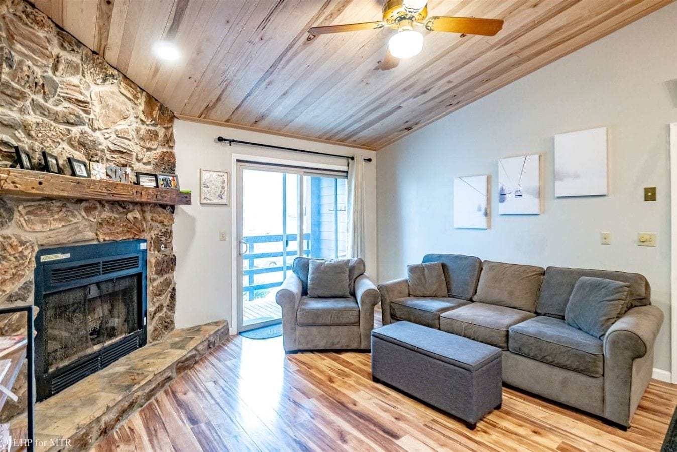 A living room with a stone fireplace, a sofa set, and a ceiling fan.