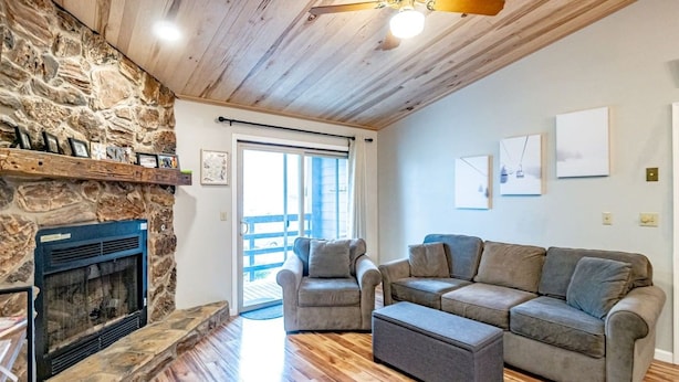 A living room with a stone fireplace, a sofa set, and a ceiling fan. - Salty Peaks - Slopeside C301 (Tucker County)