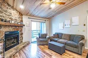 A living room with a stone fireplace, a sofa set, and a ceiling fan.