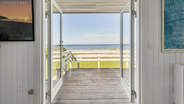 Eine offene Tür, die auf ein Holzdeck mit Meerblick führt.