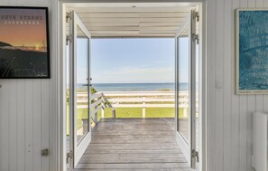 An open doorway leading to a wooden deck with a view of the ocean.