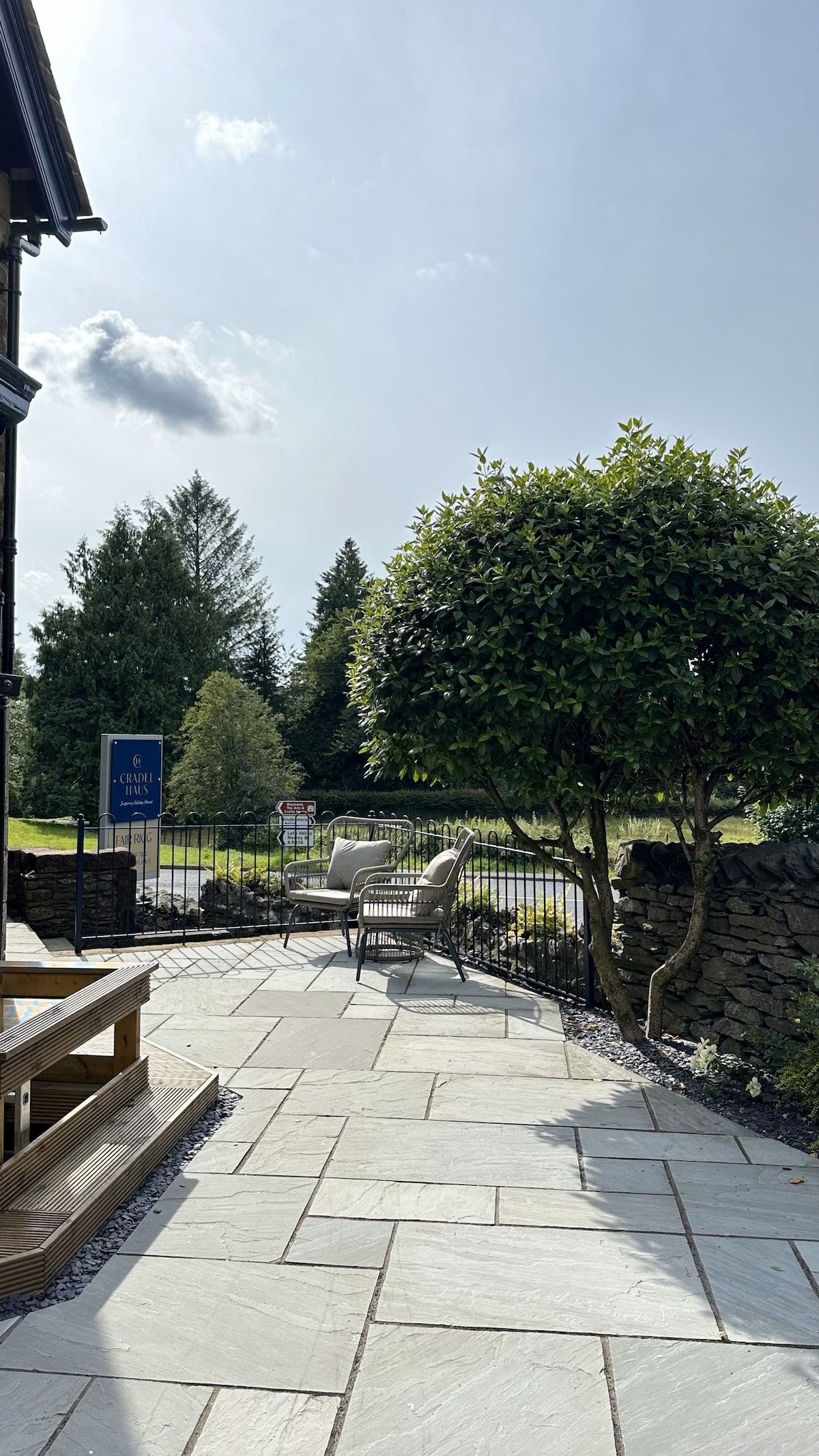 An outdoor patio area with stone flooring, a wooden bench, and a metal fence.