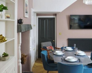 Un coin repas avec une table dressée pour quatre personnes, des chaises, un téléviseur fixé au mur et une porte donnant sur une autre pièce.
