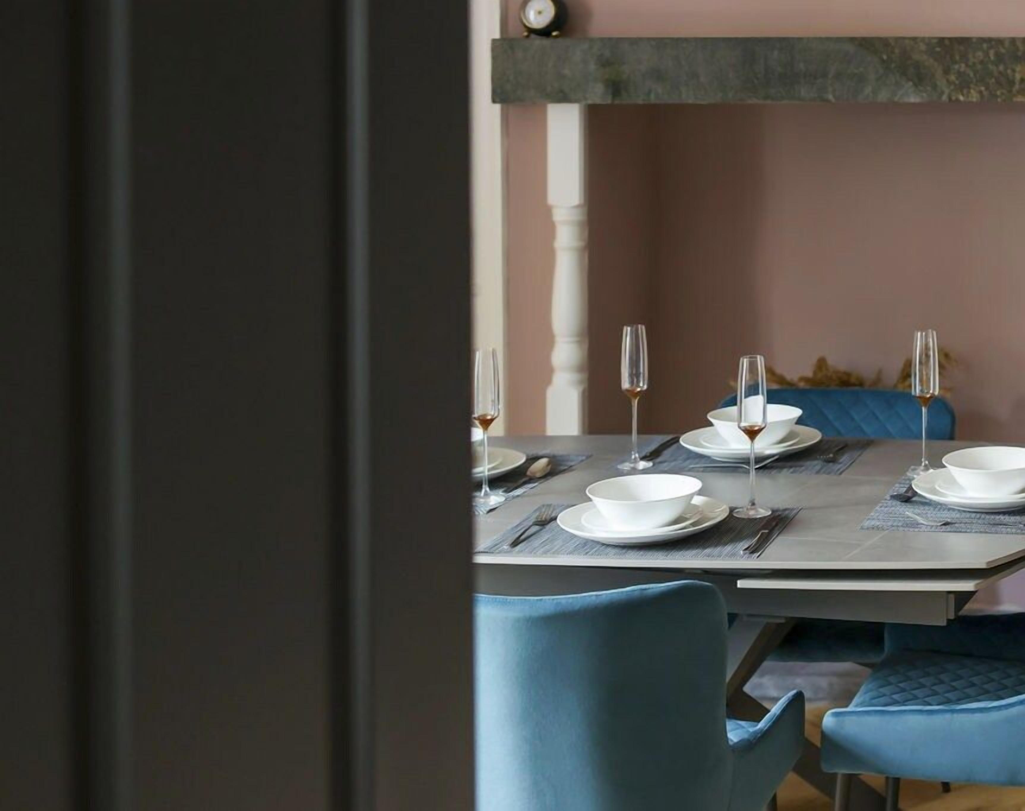 Indulge in elegance at Wainwright Apartment – a glimpse of the dining table set for four with teal velvet chairs and champagne flutes. Extendable for six, offering chic versatility.