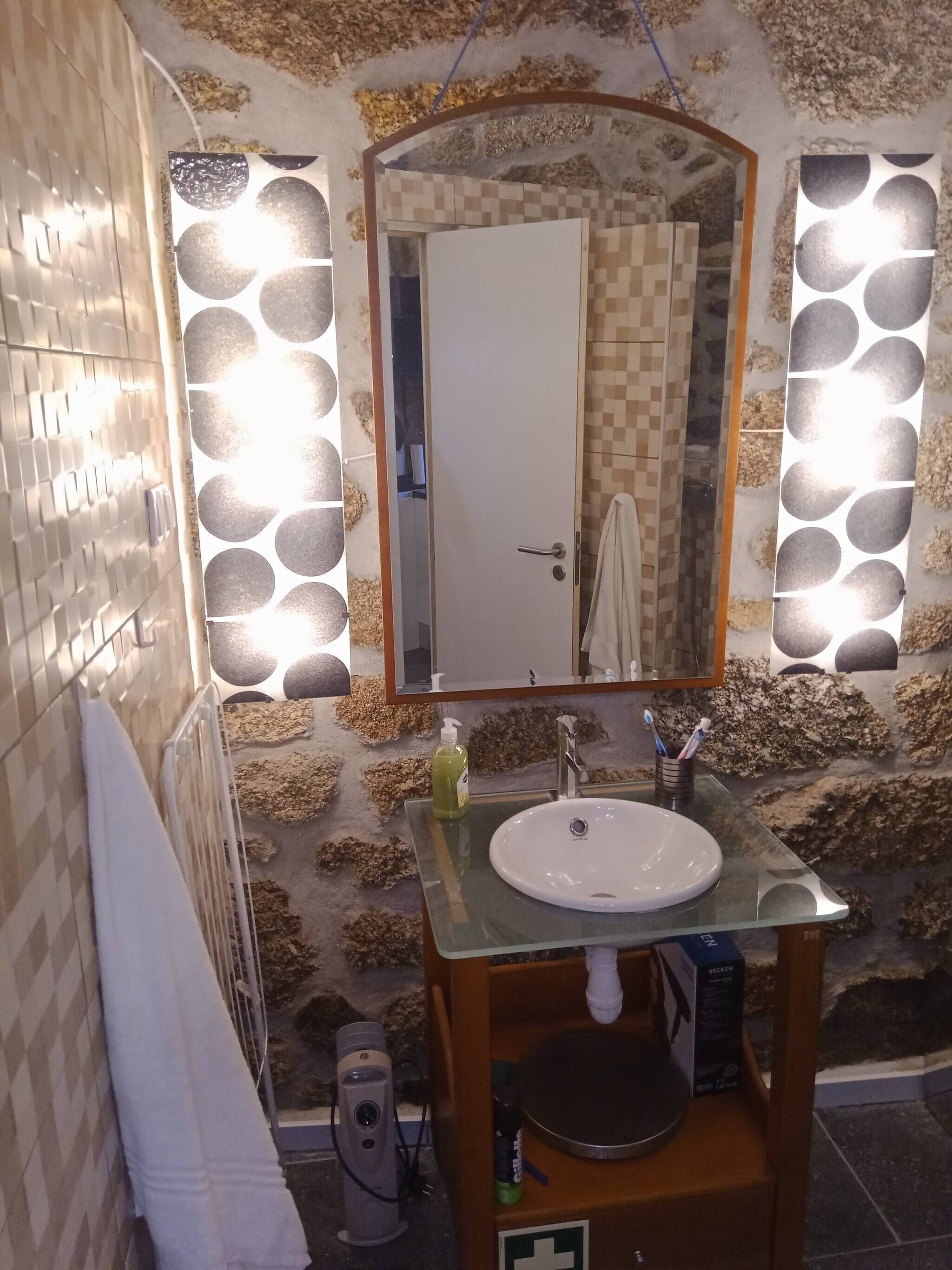 A bathroom with a stone wall, a glass sink vanity, and a mirror.