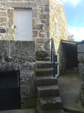 A stone building with a white door, a welcome sign, and a staircase leading to an upper level. - Cottage Aldeia Da Serra - Historic Areas of Portugal (Celorico da Beira)