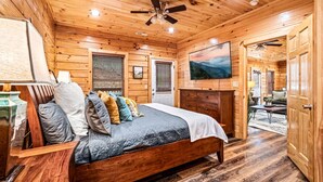 A wooden cabin bedroom with a bed, a ceiling fan, and a painting on the wall. - 5BD: Prime Pigeon Forge with 2 Hot Tubs, Pool Table, Theater, Arcade and 3 Decks (Pigeon Forge)