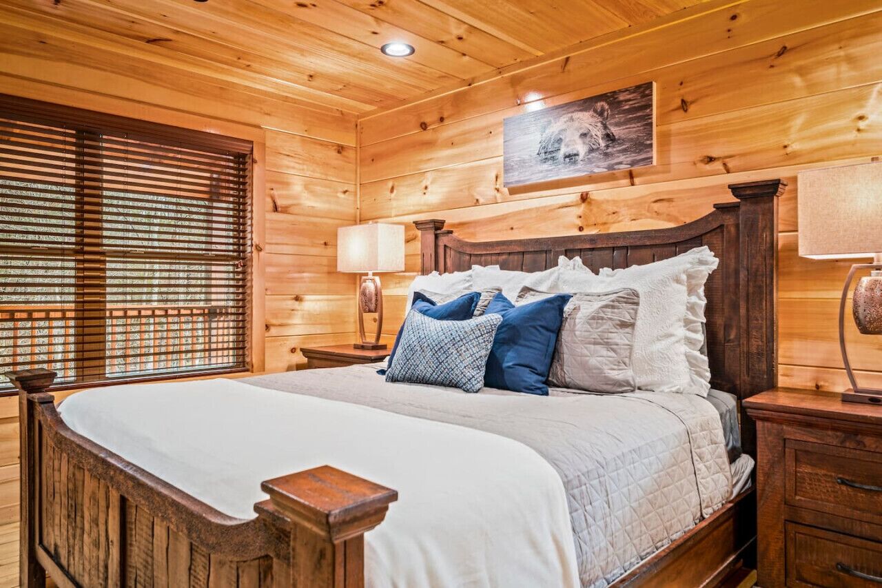 Een slaapkamer in een houten chalet, met een bed, een nachtkastje, een lamp en een raam met zonwering.
