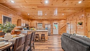 A wooden cabin interior with a dining area, kitchen, and living space. - 5BD: Prime Pigeon Forge with 2 Hot Tubs, Pool Table, Theater, Arcade and 3 Decks (Pigeon Forge)