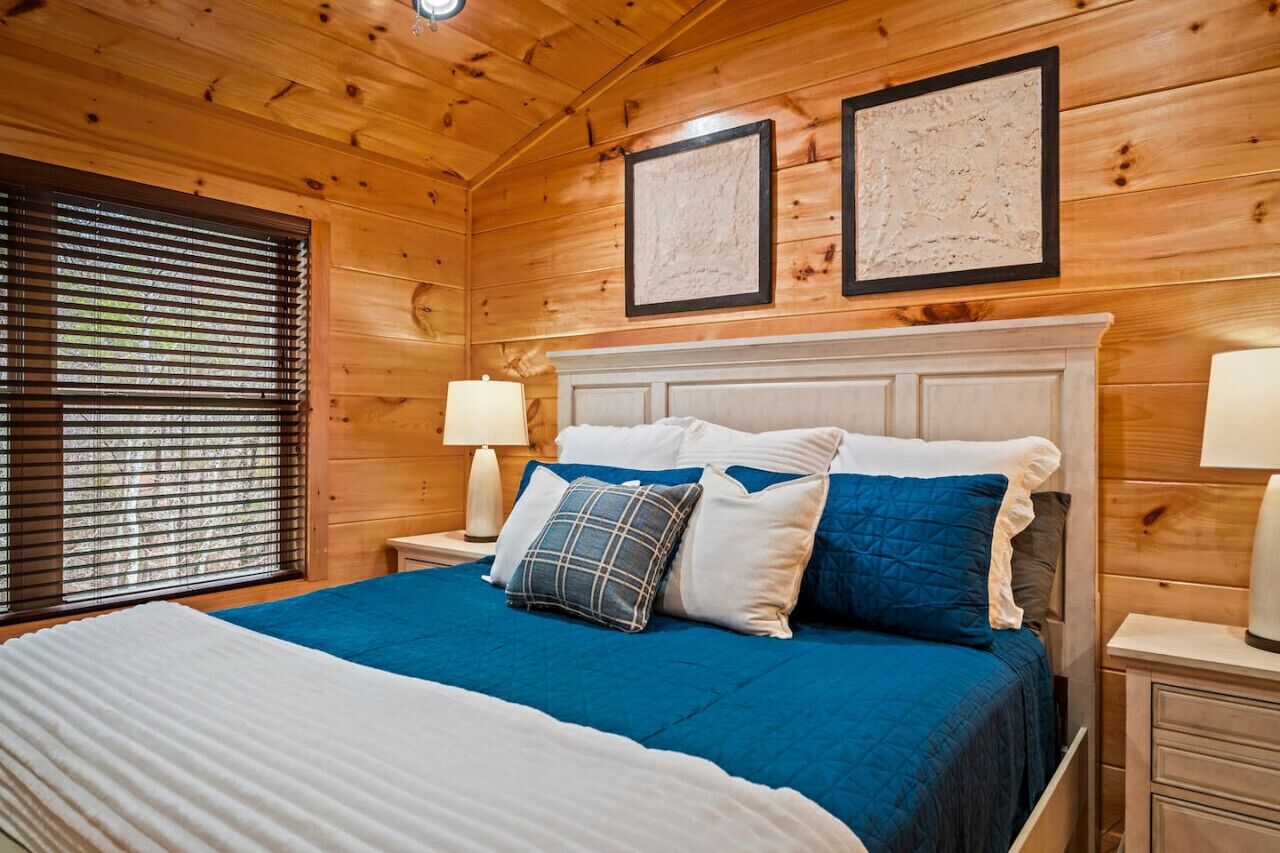 Un dormitorio de cabaña de madera con una cama, dos cuadros enmarcados y una mesita de noche con lámpara.