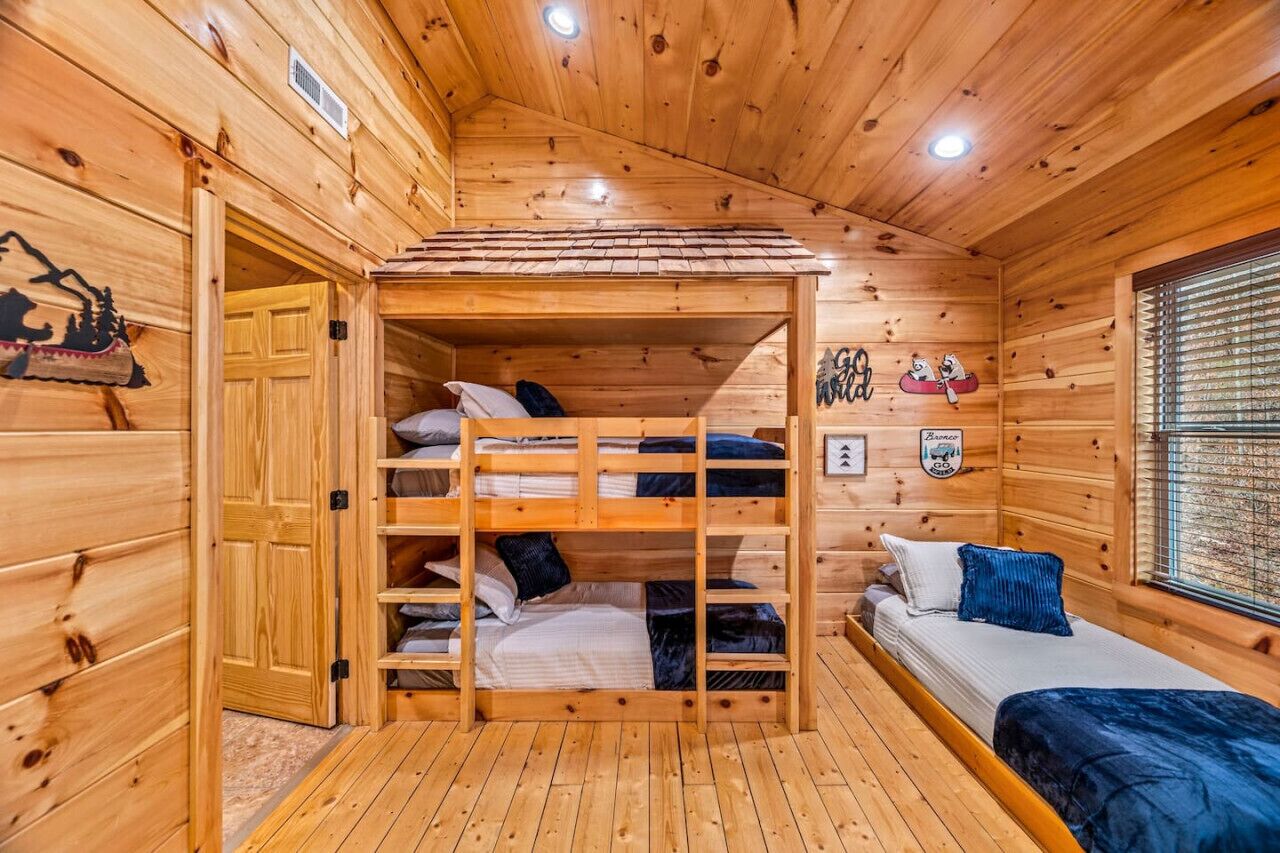Interior de una cabaña de madera con literas, un ventanal pequeño y una puerta.